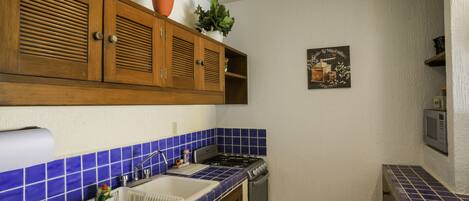 A kitchen with blue-tiled backsplash, wooden cabinets, a gas stove, and a sink.