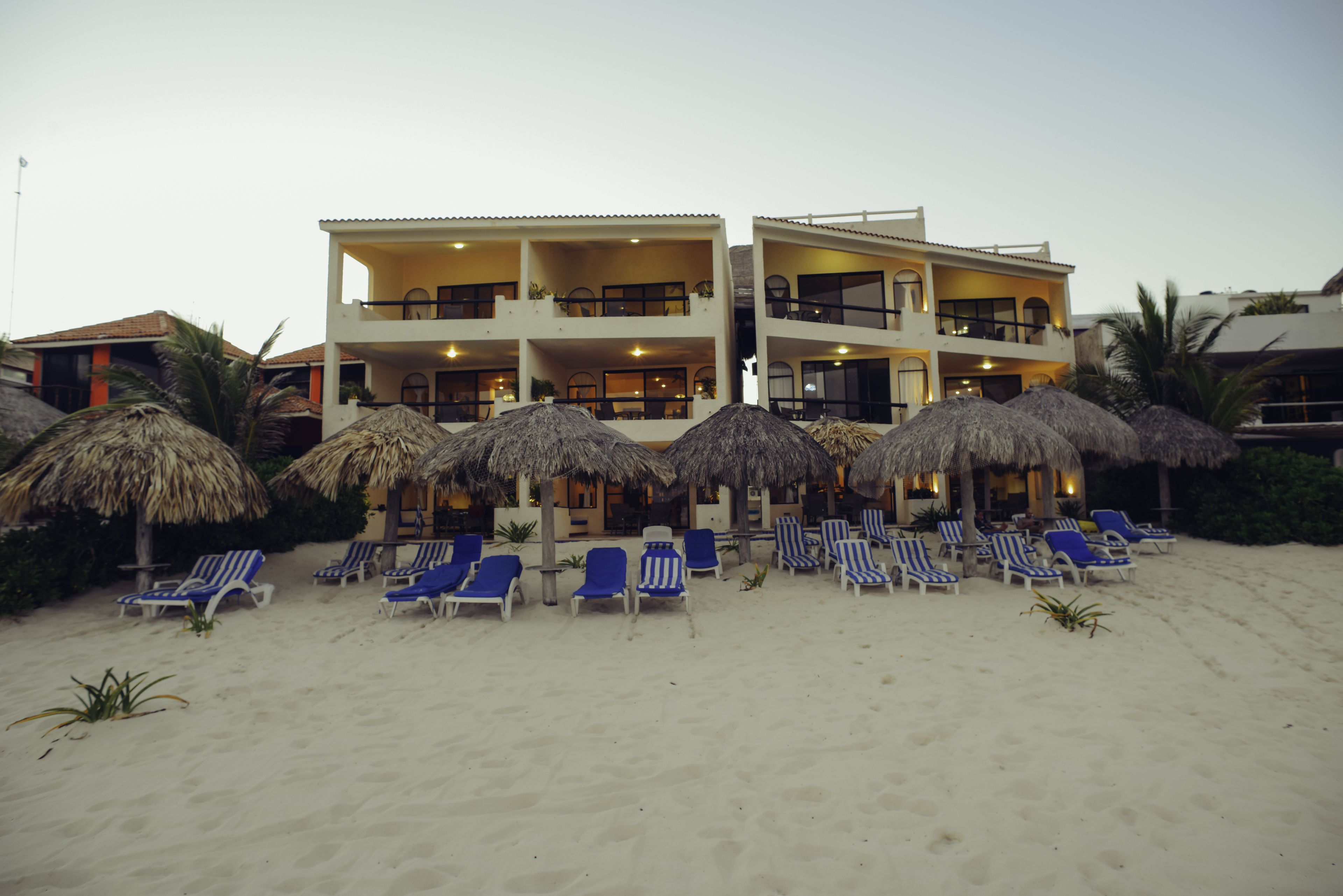 A beachfront hotel with multiple balconies, sun loungers, and thatched umbrellas.