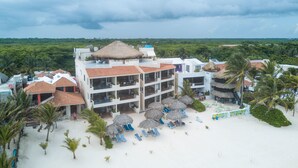 Un resort con varias edificaciones, una zona de playa con tumbonas y sombrillas, y vistas al follaje circundante.
