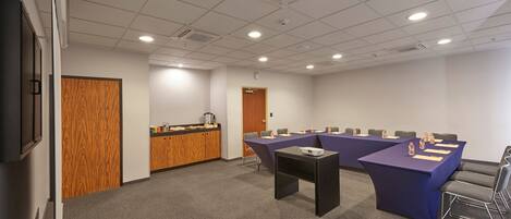 Una sala de conferencias con una larga mesa, sillas, un proyector y una pequeña mesa con una pantalla.