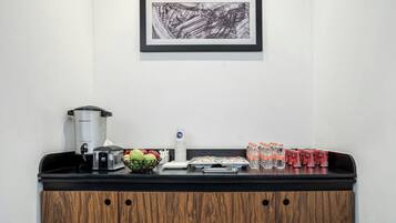 Una kitchenette con cafetera, tostadora y frutero. También hay agua embotellada y bebidas enlatadas sobre la encimera.