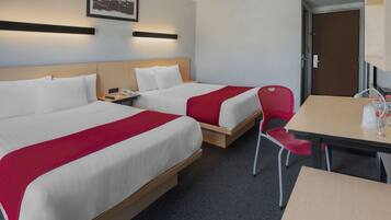A hotel room with two beds, a desk, and a chair. There is a door and a framed picture on the wall.
