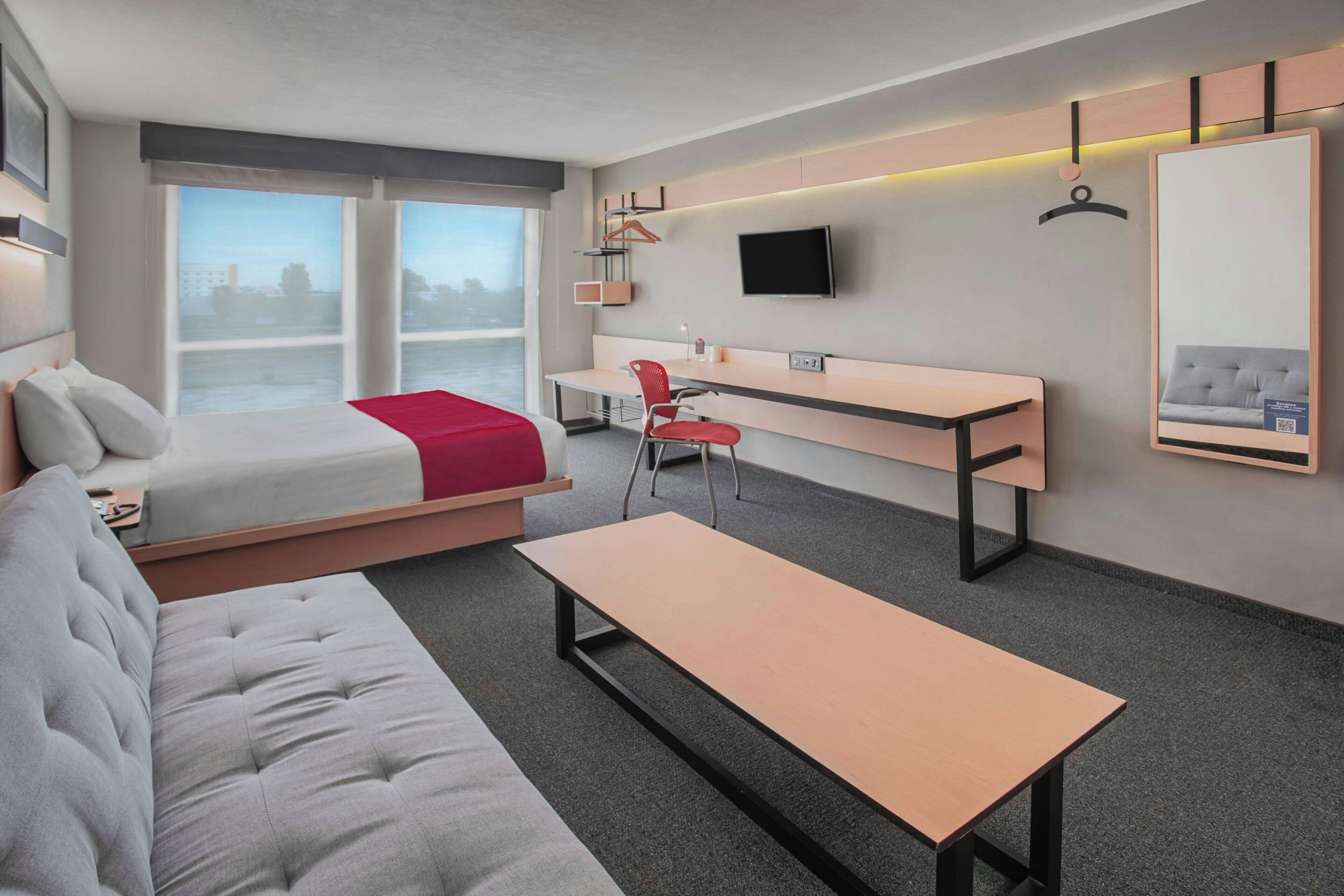 A modern hotel room with a bed, a sofa, a desk, and a TV.