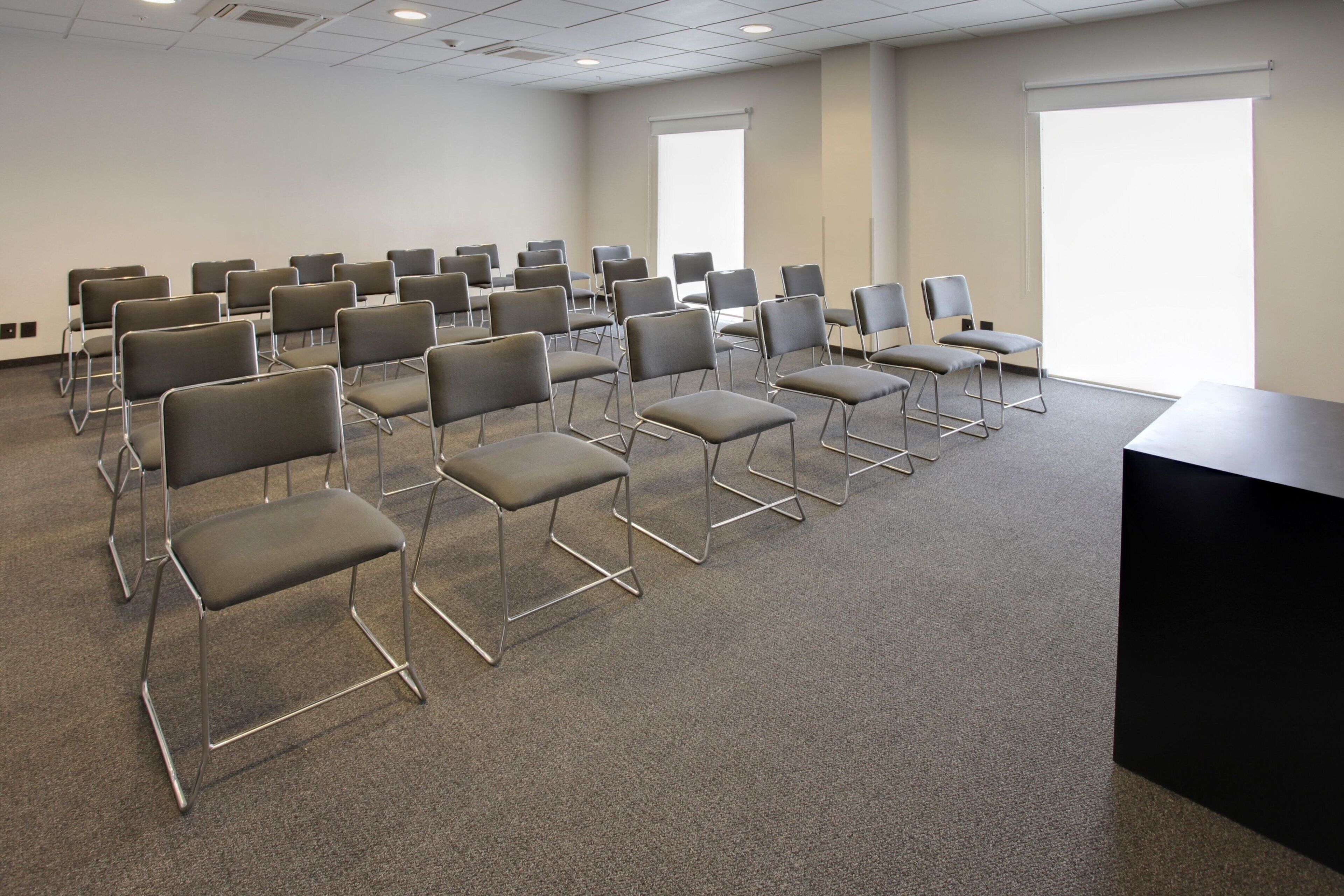 A conference room with rows of chairs, a black table, and large windows.