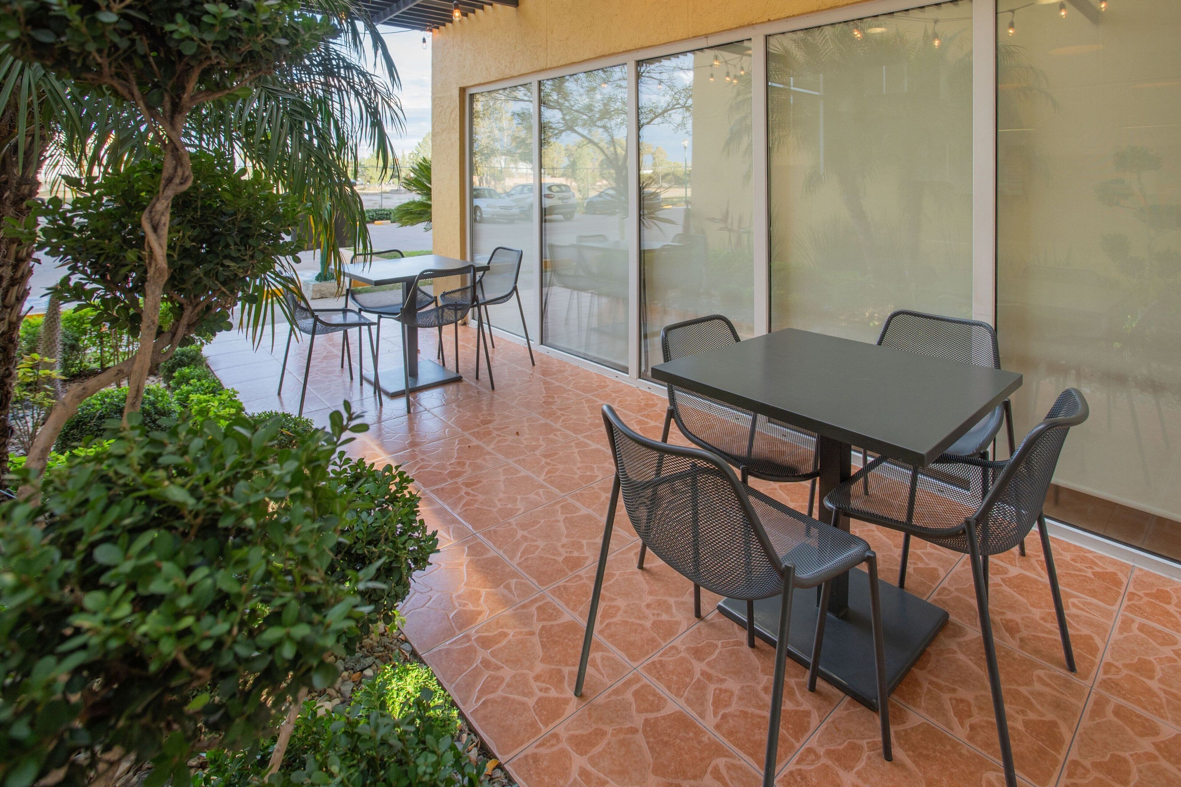 An outdoor patio with a table and chairs, surrounded by greenery and a tiled floor.