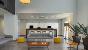 A modern lobby with a sofa, two coffee tables, a reception desk, and a large plant. - City Express by Marriott Durango (Durango)
