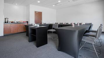 Un salón de conferencias con una mesa larga, sillas, una pequeña cocina y una puerta.