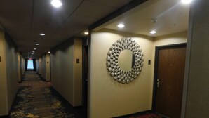 Un couloir d’hôtel avec un sol recouvert de moquette, une décoration murale circulaire et des portes situées à droite.