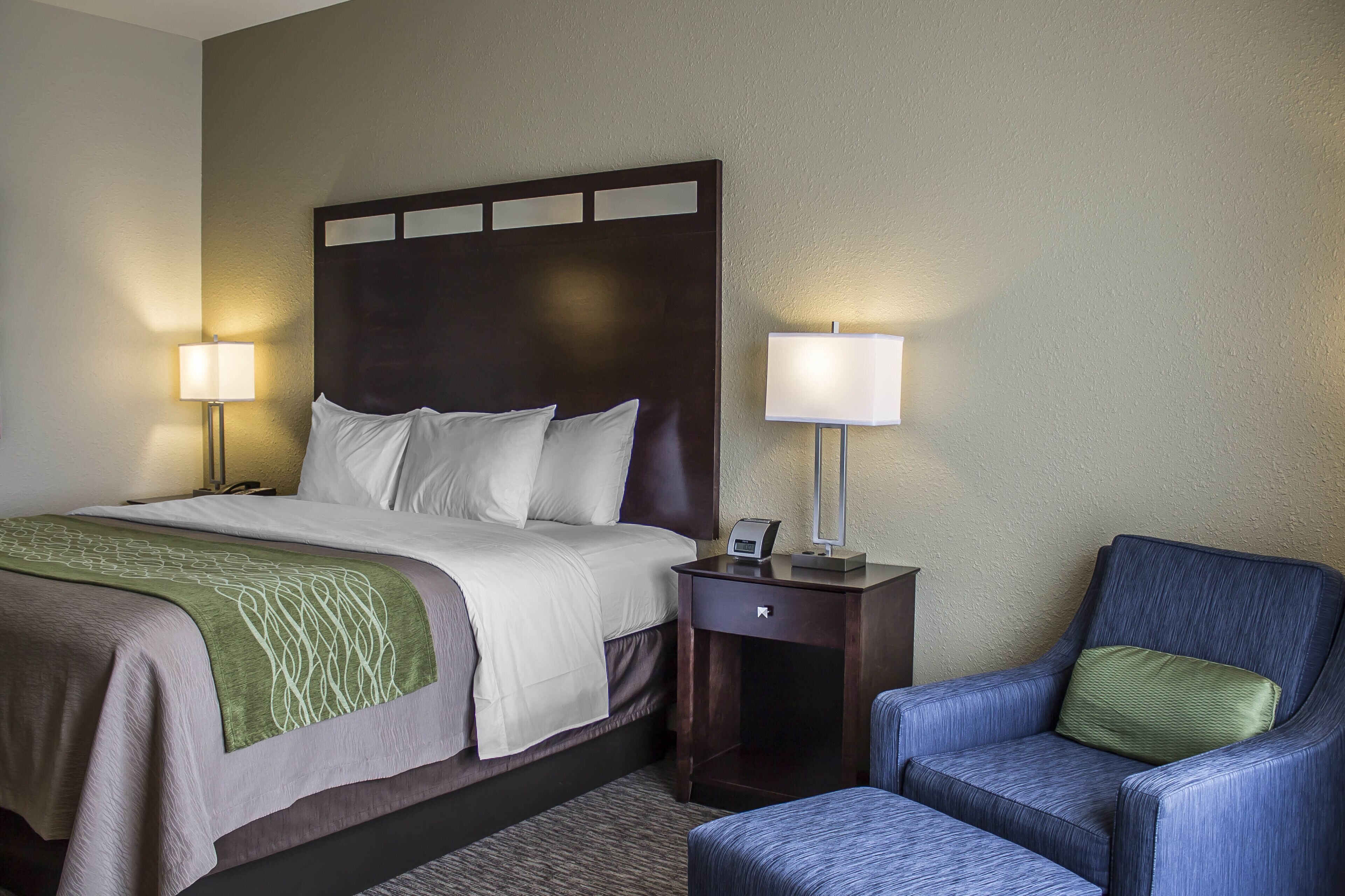 A hotel room with a bed, bedside tables, a chair, and a lamp.