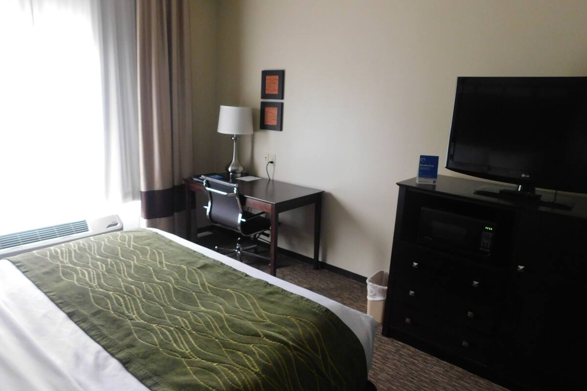 A hotel room with a bed, a desk, a chair, a television, and a lamp.