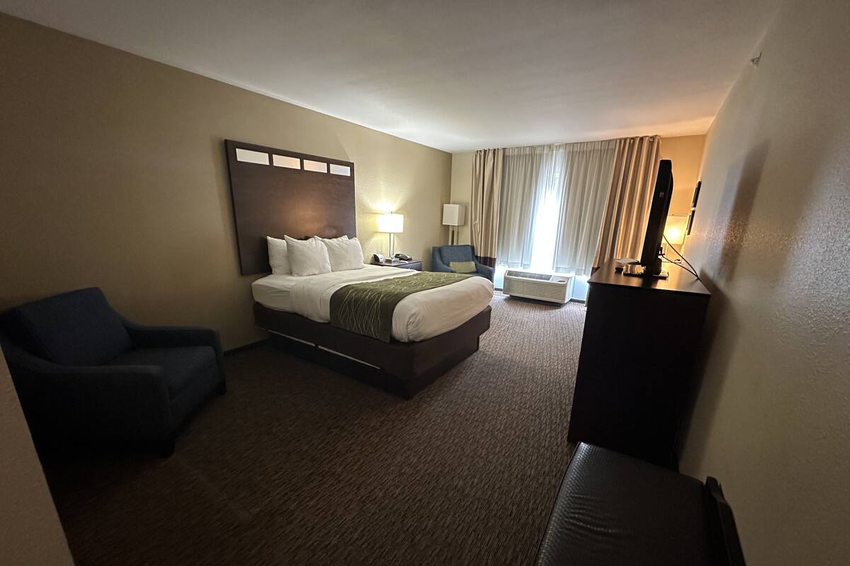 A hotel room with a bed, a chair, a desk, a lamp, and a television.