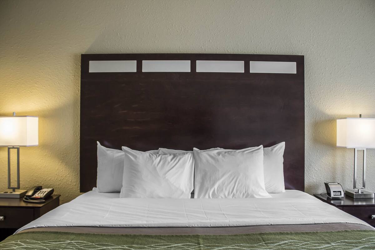 A hotel room with a large bed, two bedside tables, a nightstand, and a wall-mounted lamp.