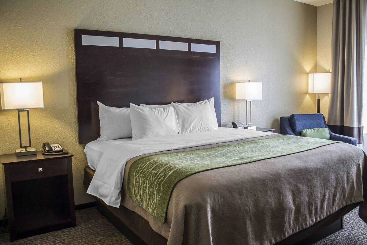 A hotel room with a large bed, two bedside tables, a nightstand, a chair, and two lamps.