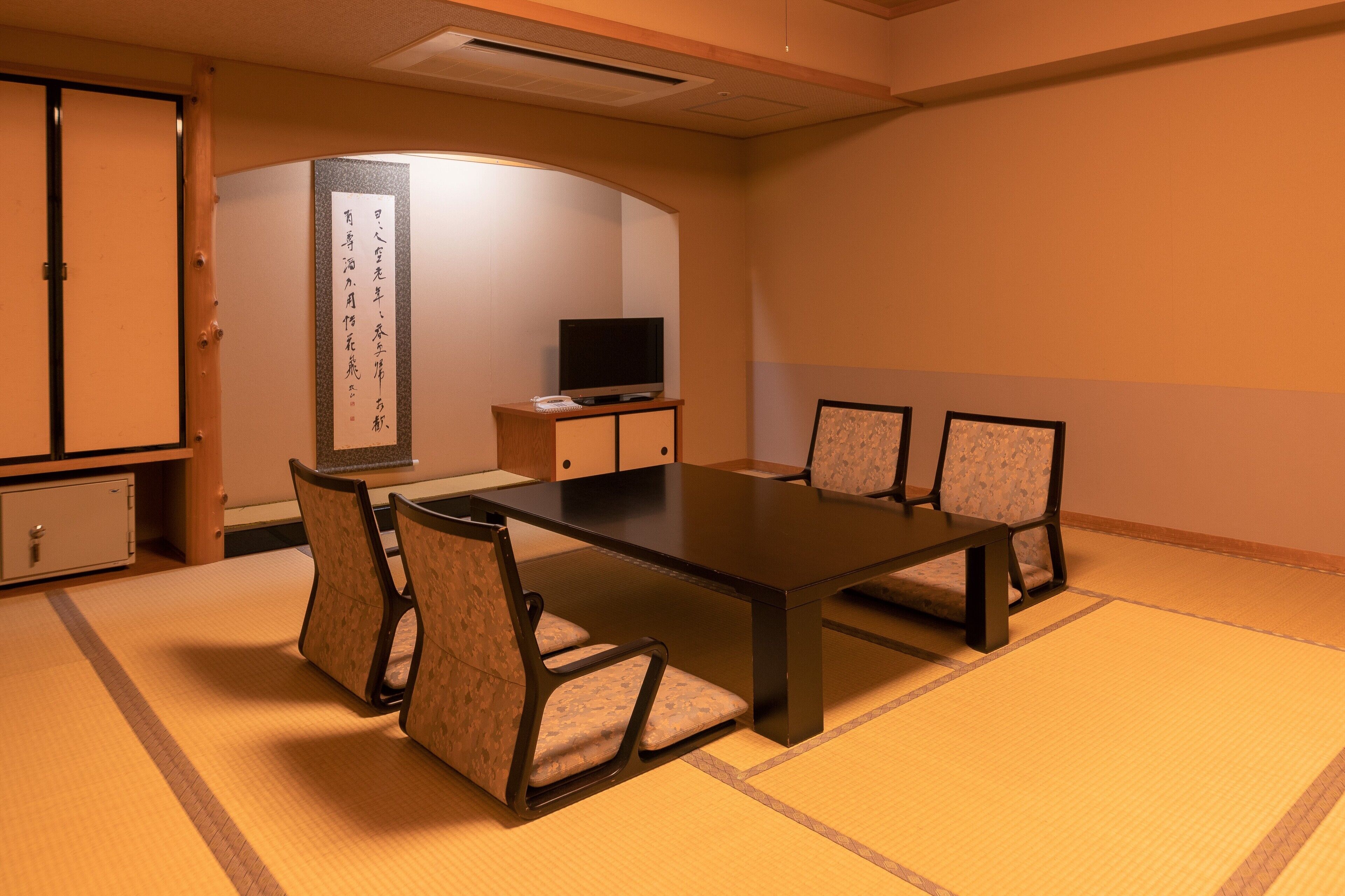 Een vergaderruimte met een lange tafel, zes stoelen, een televisie op een kast en een traditionele Japanse kalligrafiewerk op de muur.
