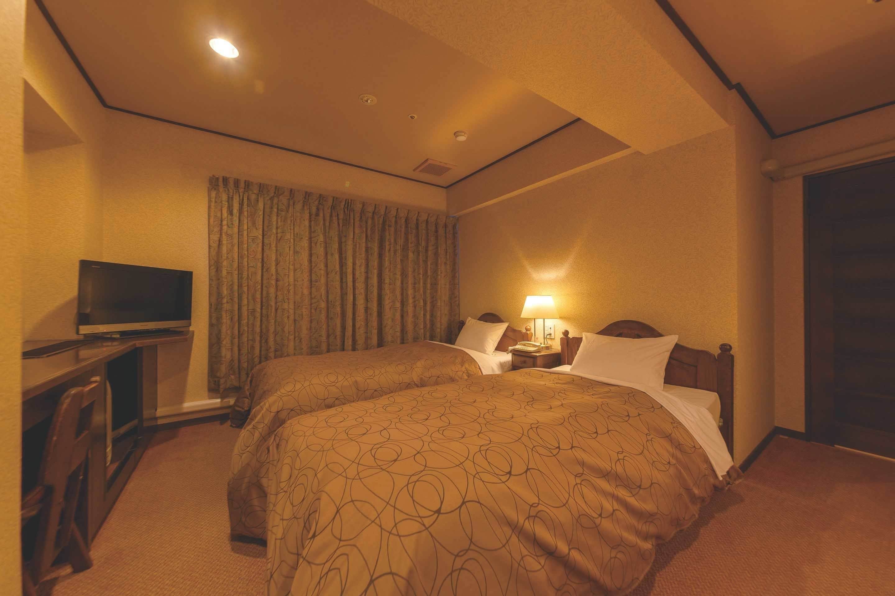 A hotel room with two beds, a television, a desk, and a lamp.