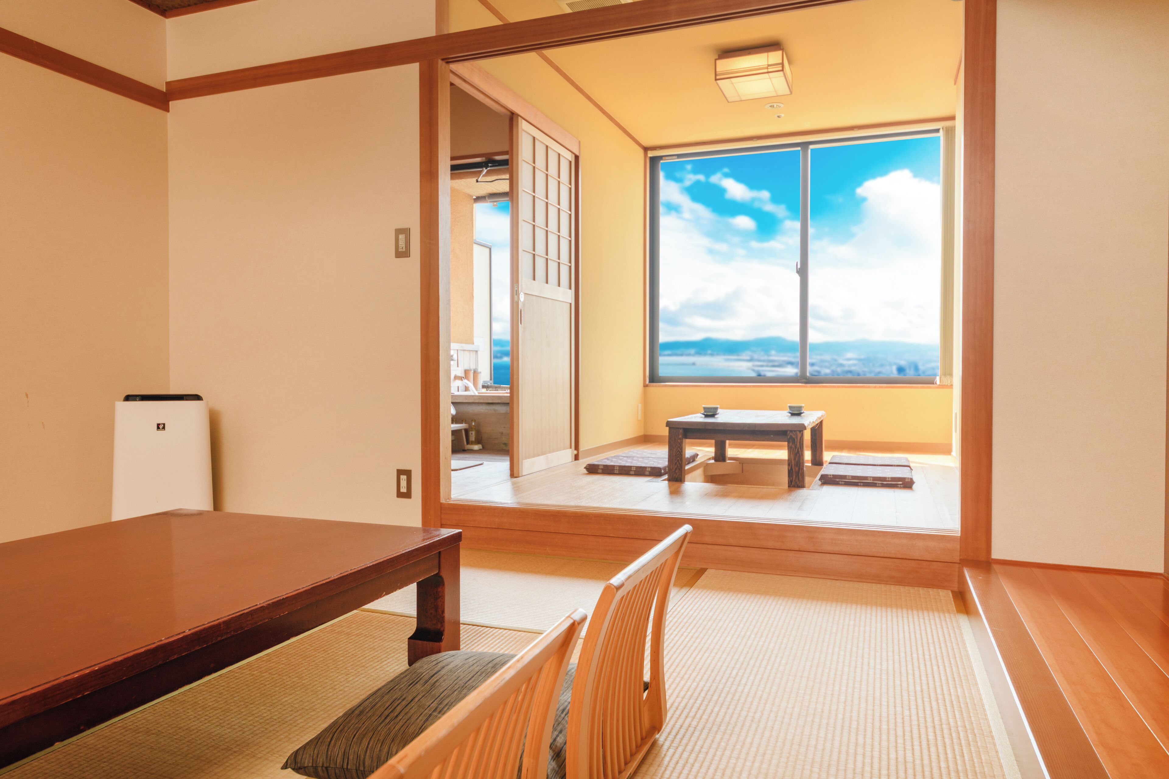 A traditional Japanese room with tatami flooring, a low wooden table, and a sliding door leading to a balcony with a view.