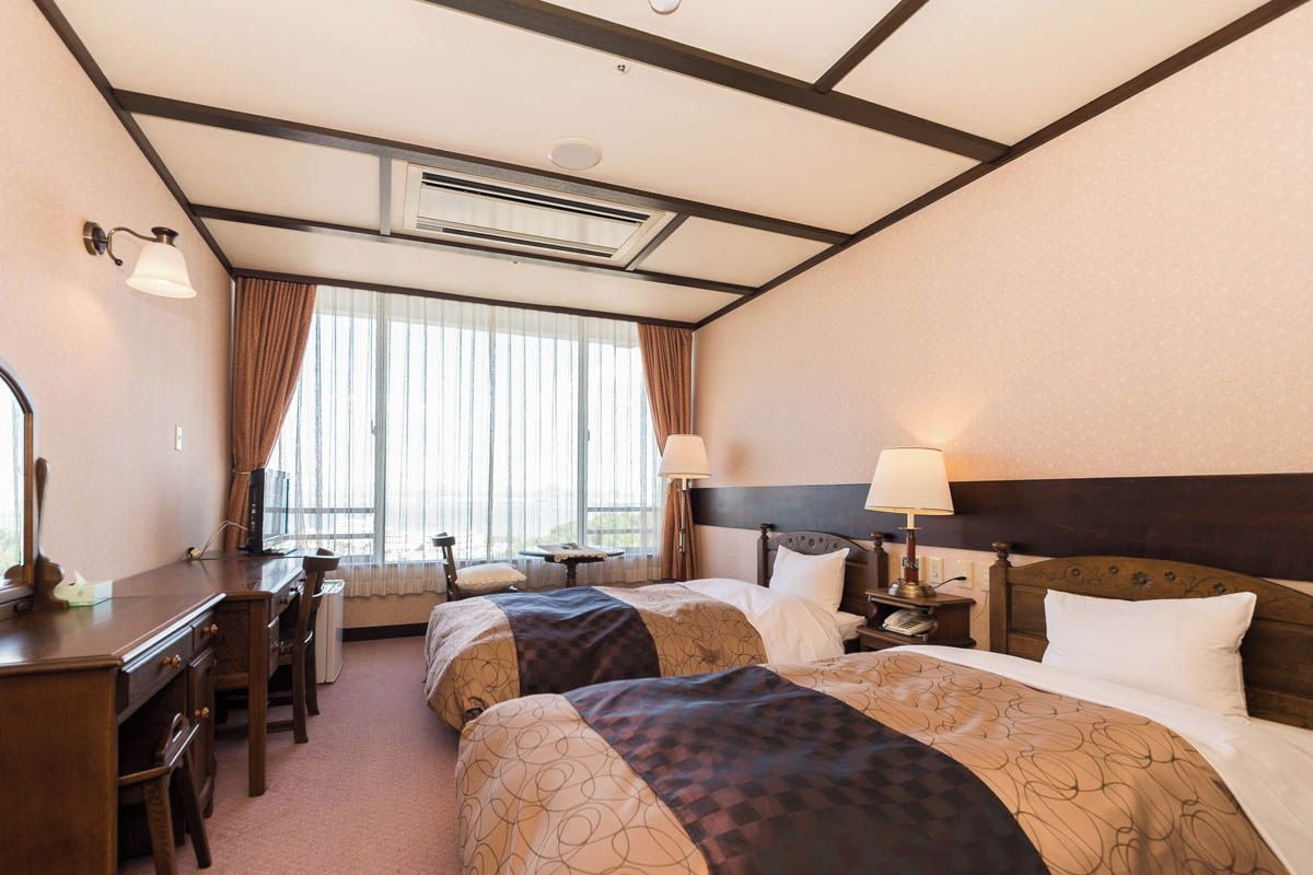 A hotel room with two beds, a desk, a chair, and a window with curtains.