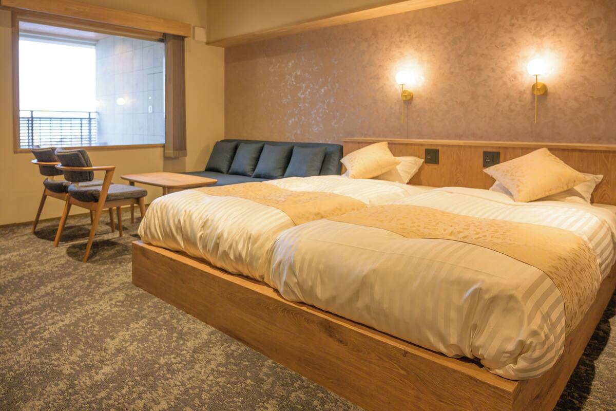 A hotel room with a large bed, a seating area with chairs, a small table, and two wall-mounted lights.
