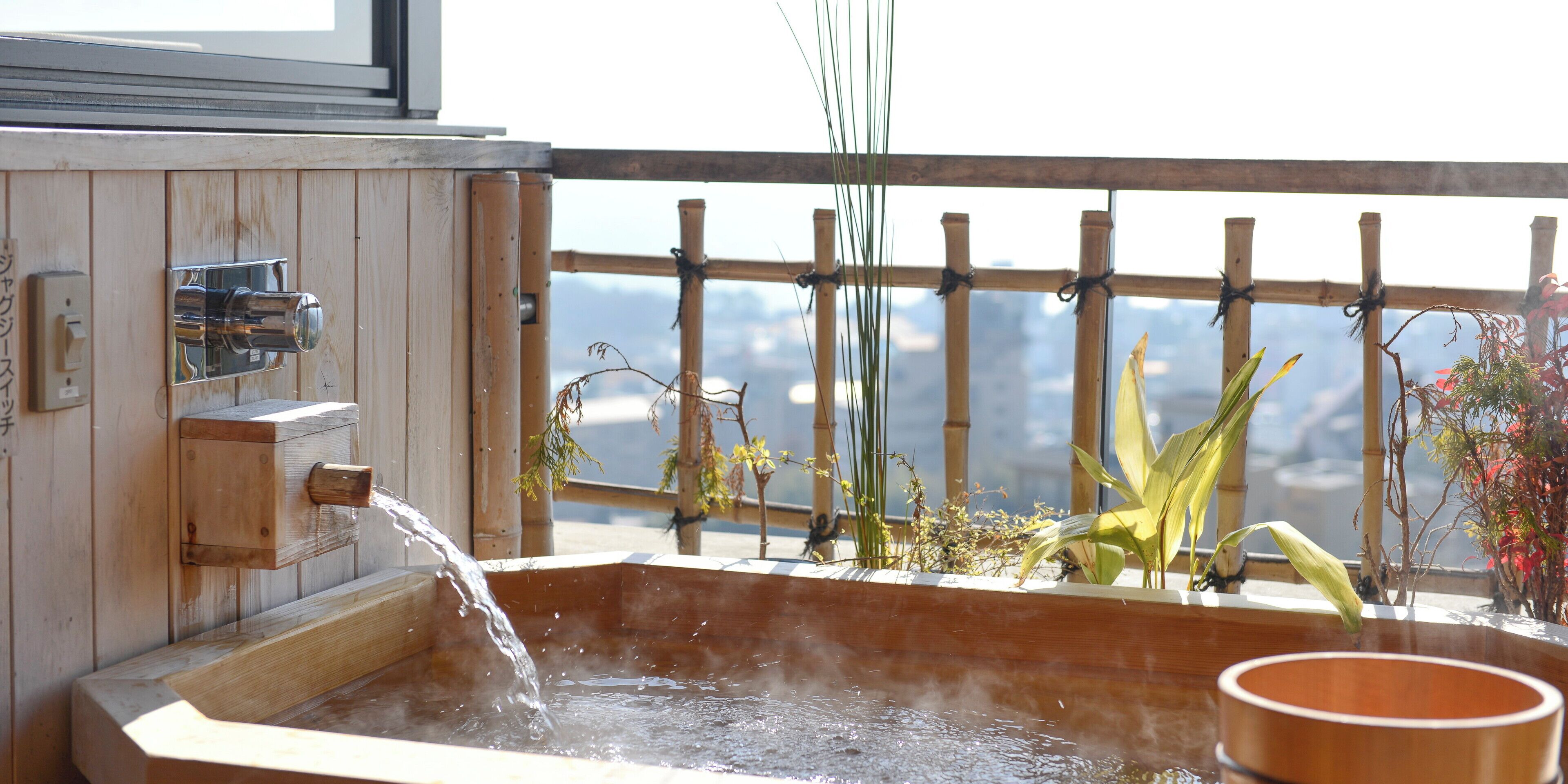 Un baño de aguas termales de madera con barandilla de madera y plantas.