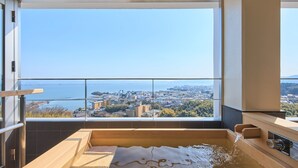 A modern bathroom with a large bathtub, a view of a cityscape, and a balcony with a railing. - Satoyu Mukashibanashi Yuzanso Ryokan (Otsu)