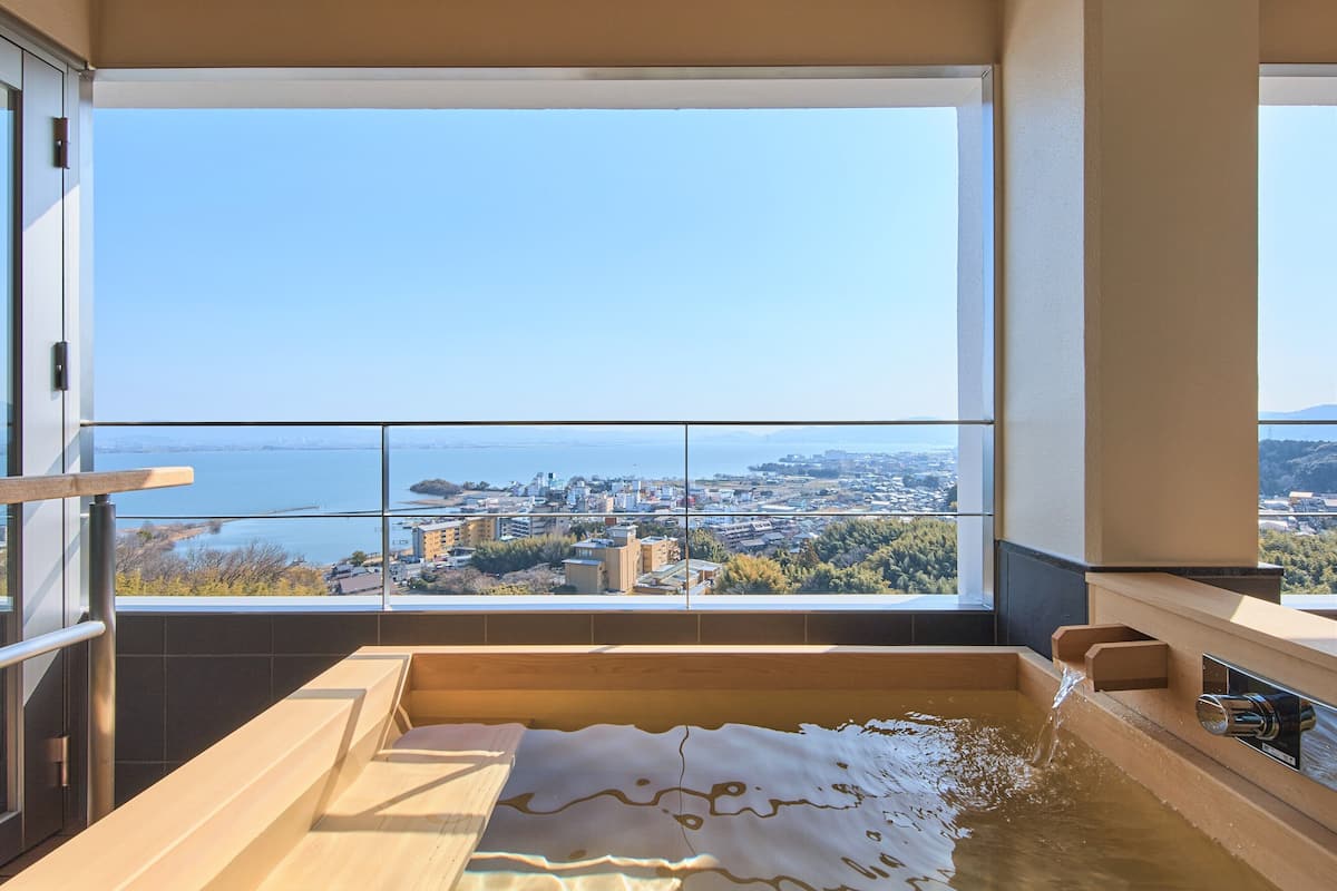 A modern bathroom with a large bathtub, a view of a cityscape, and a balcony with a railing.