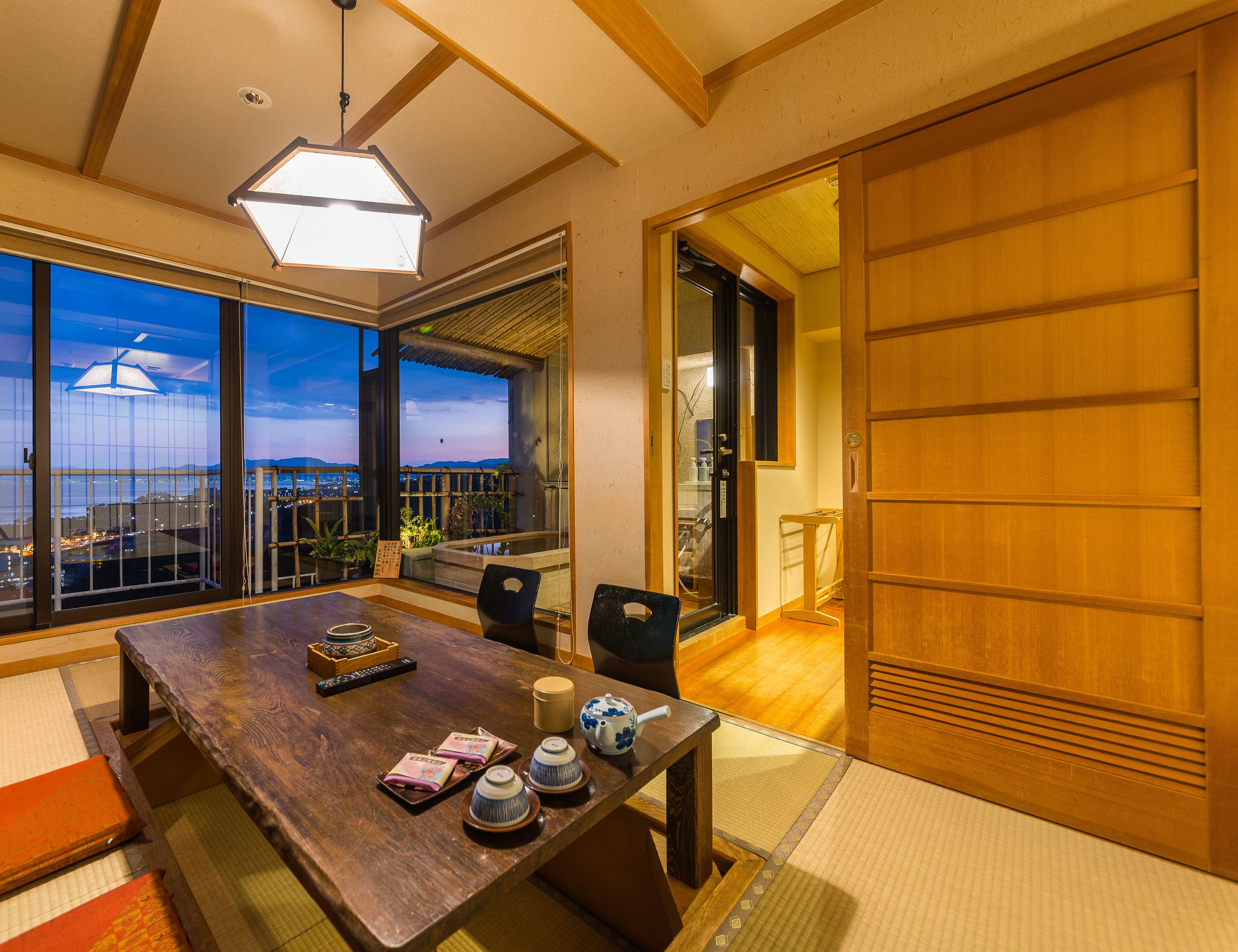 A traditional Japanese-style room with tatami flooring, a wooden table with tea set, and a sliding door leading to another room.