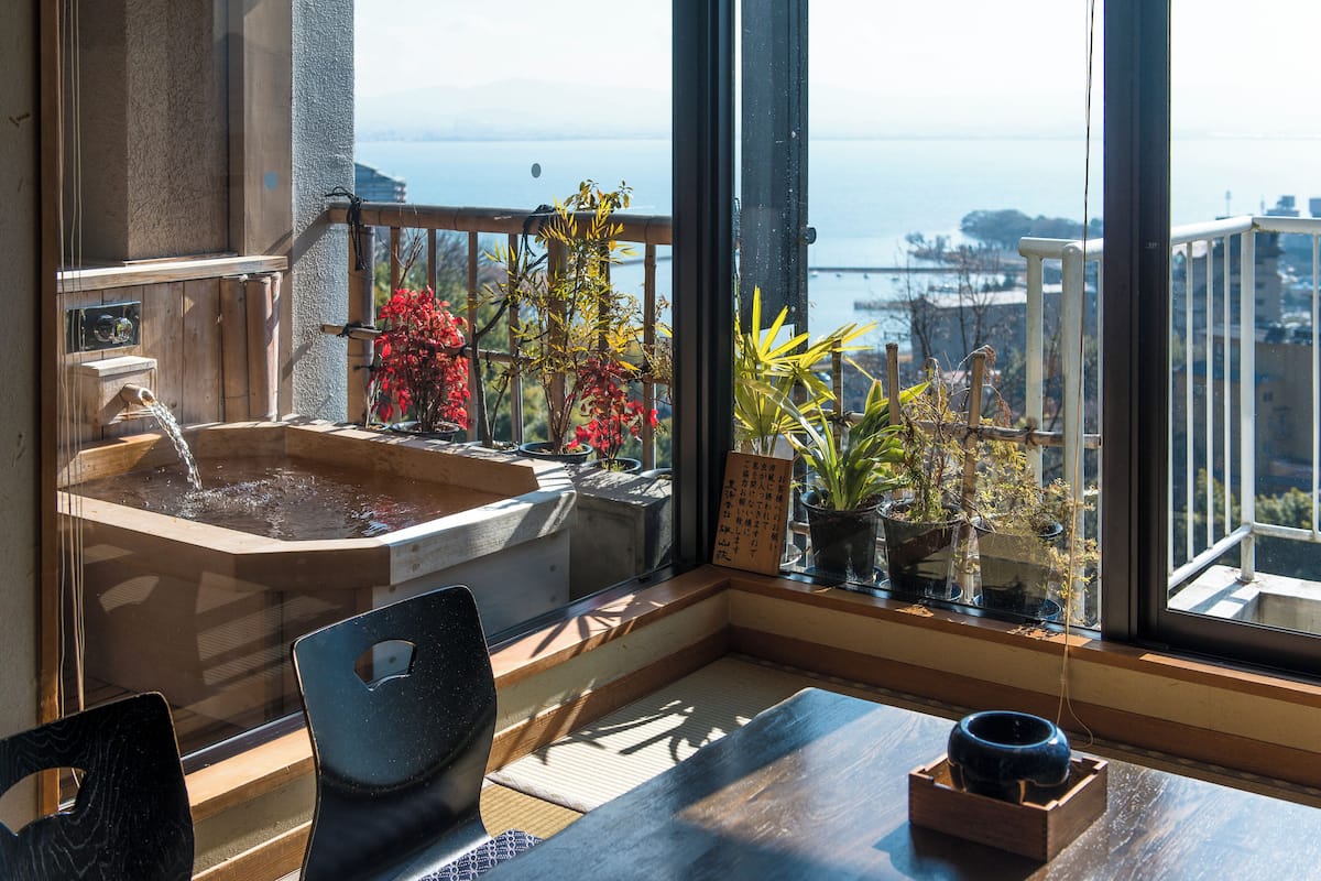 A room with a wooden table, a chair, a small water feature, and potted plants.