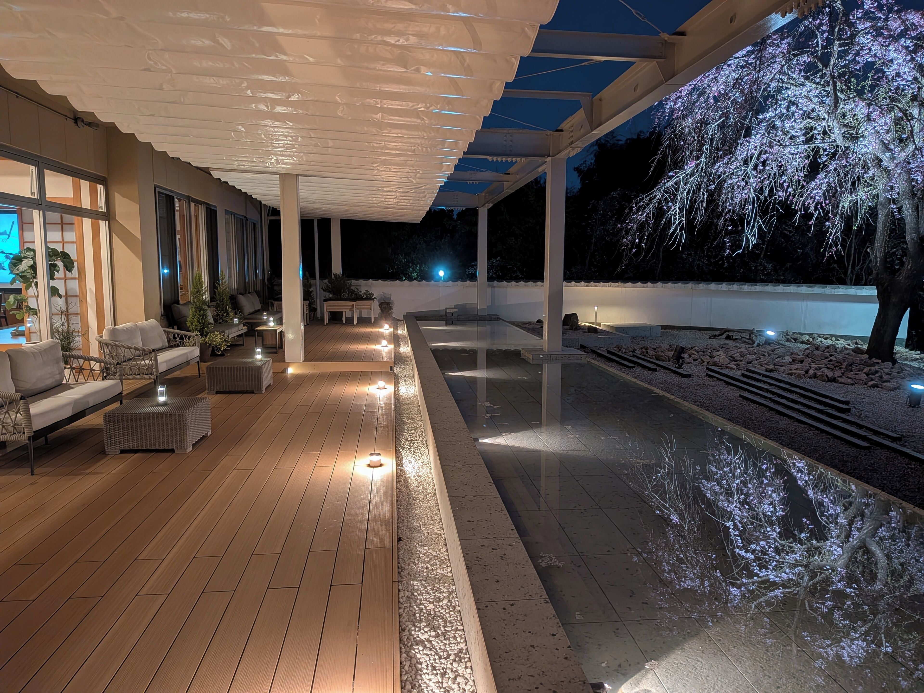 A covered outdoor area with wooden flooring, seating, and a pool.