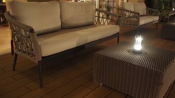 Un juego de sofá y sillón de mimbre sobre una terraza de madera, con un farol en una mesa tejida.