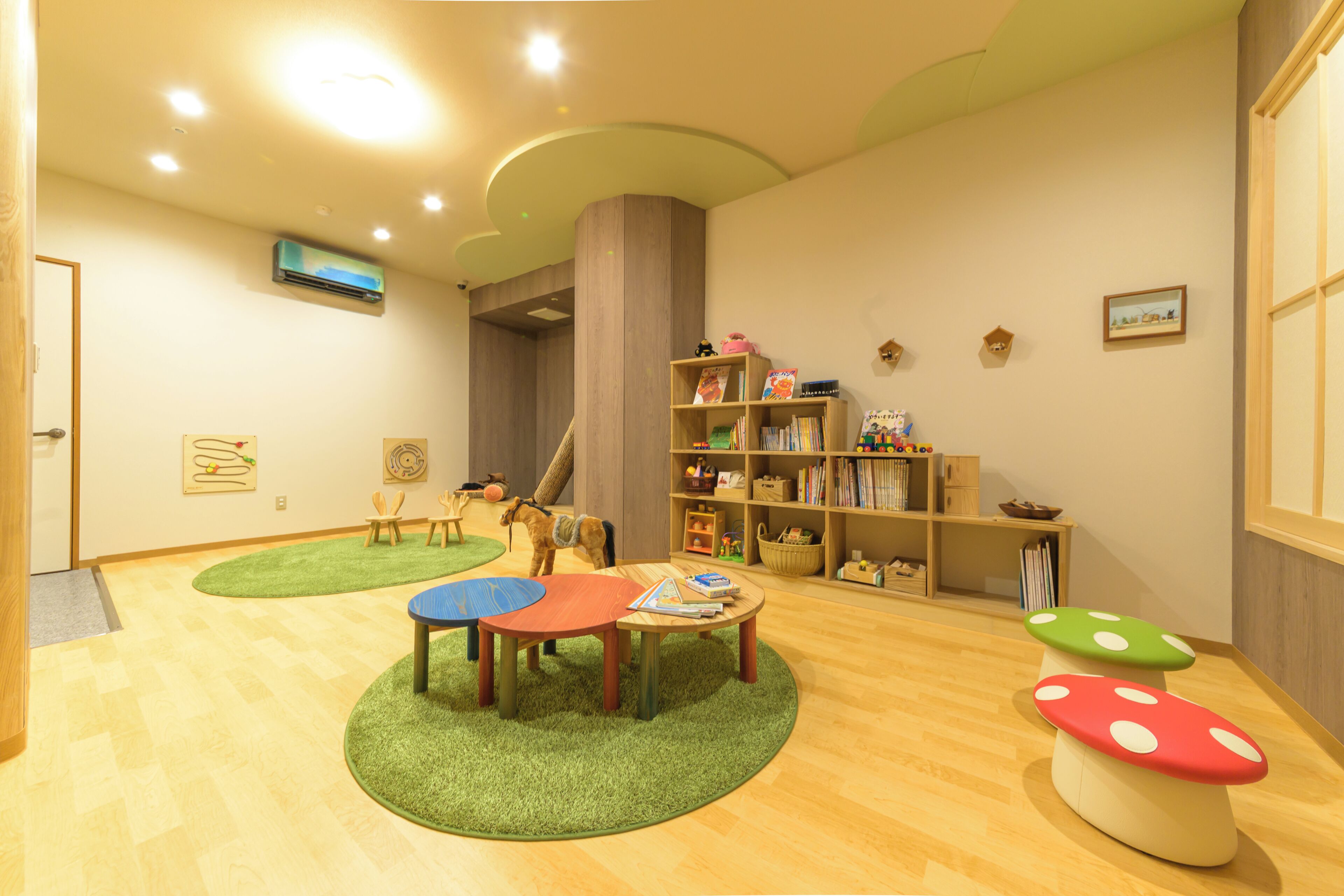 Une pièce avec un plancher en bois, une moquette verte, une bibliothèque, une petite table et un cheval en jouet.