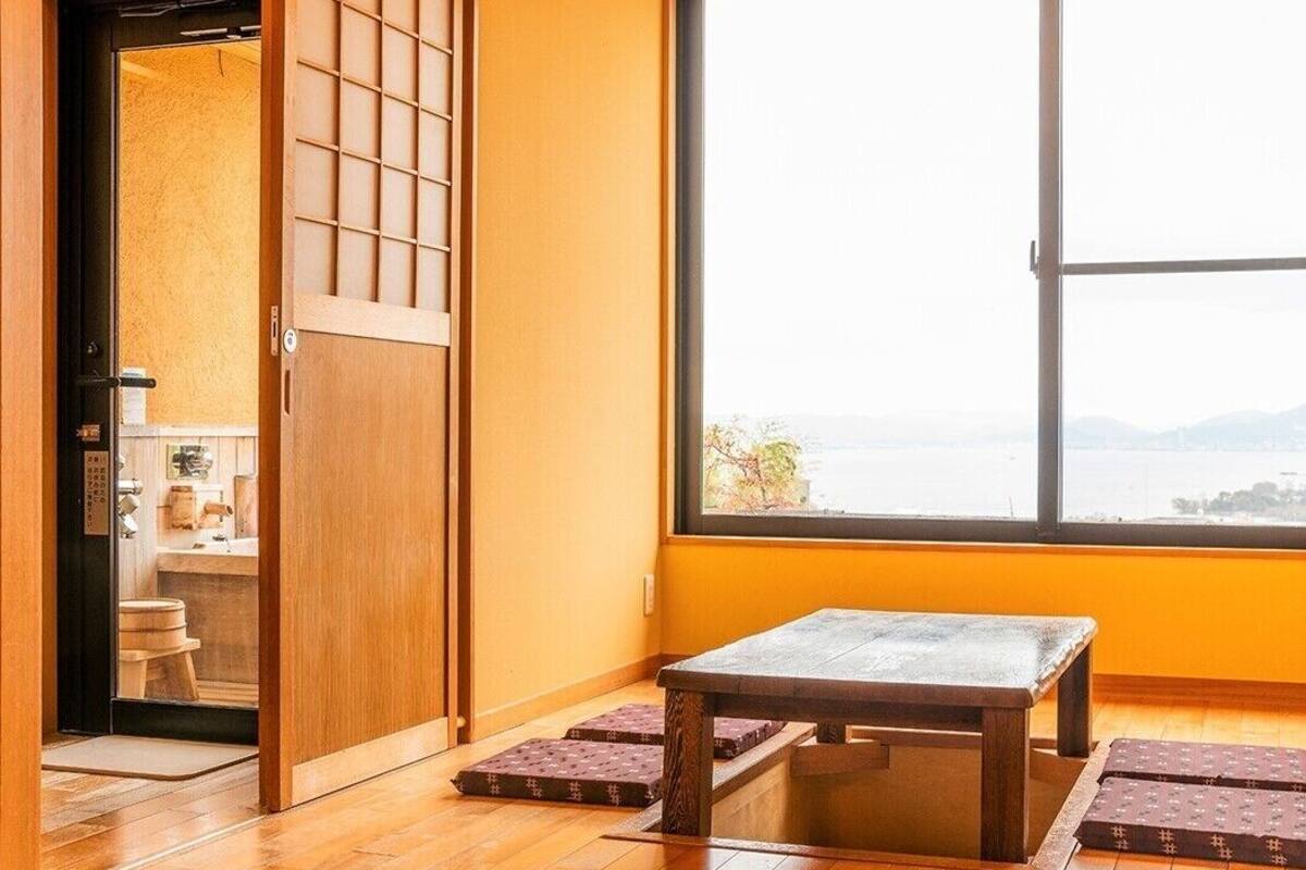 A traditional Japanese room with tatami flooring, a wooden table, and a large window offering a view of the sea.