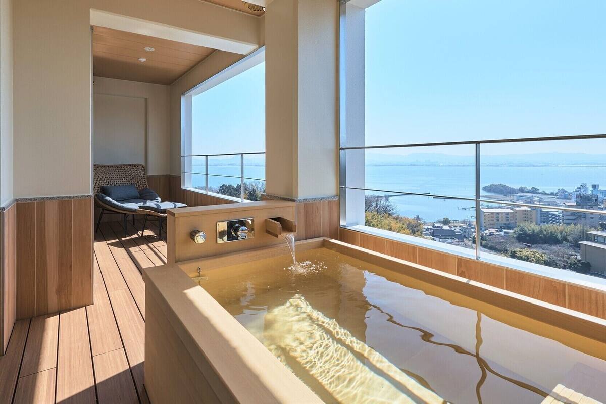 A modern bathroom with a large bathtub, wooden flooring, and a view of a cityscape and water.