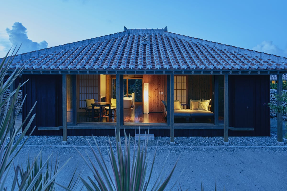 Una casa tradicional japonesa con tejado de tejas, fachada de madera y un interior acogedor con un sofá y zona de comedor.