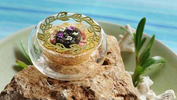 A clear glass bowl with a decorative design, placed on a textured surface with a green plate and some greenery in the background.