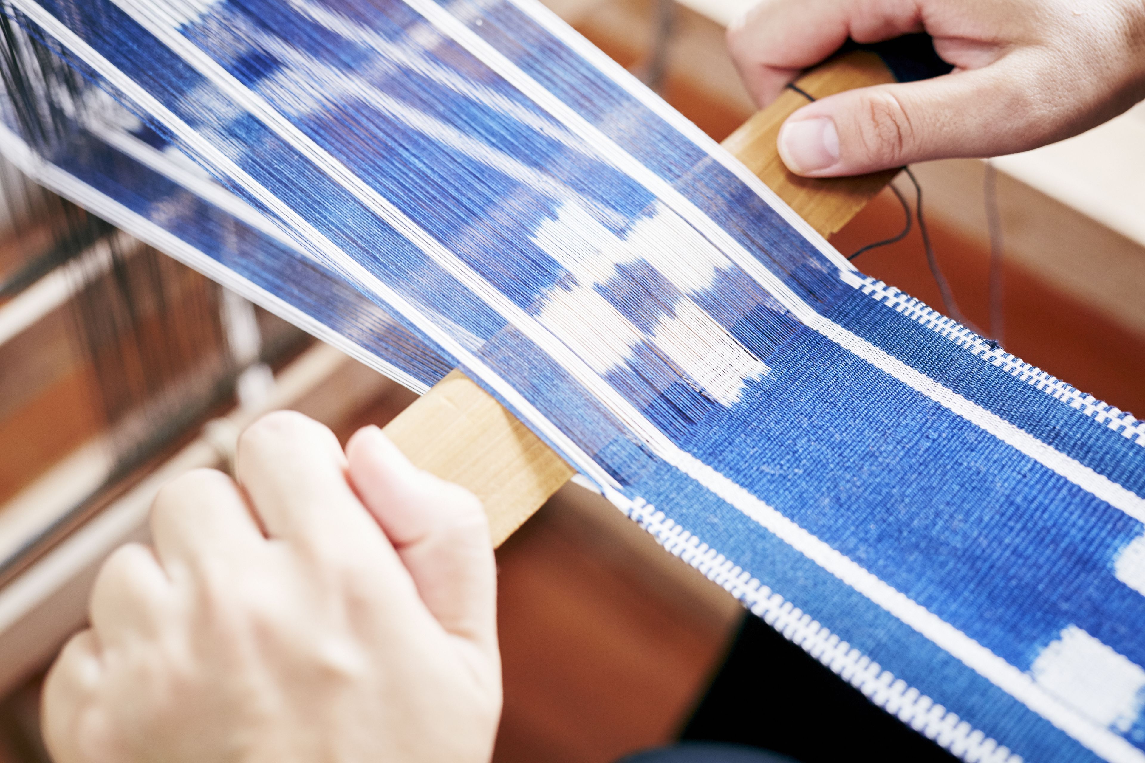A close-up of hands weaving a blue and white patterned textile.