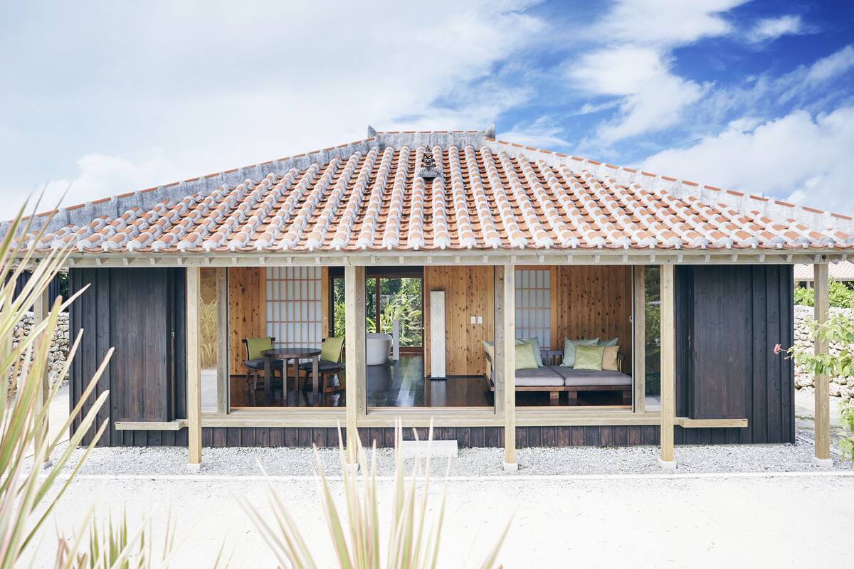 Una casa moderna con techo de tejas, fachada de madera y un porche con mobiliario.