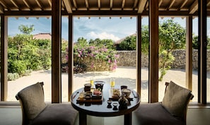 Un comedor con una mesa preparada para dos personas, con vistas a un jardín con un muro de piedra y plantas en flor.