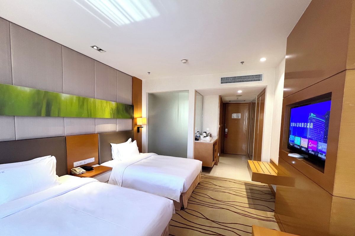 A hotel room with two beds, a TV, and a bathroom.