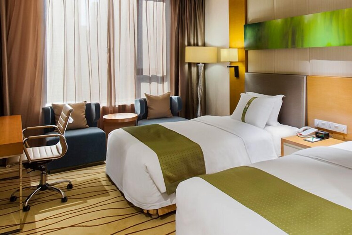 Habitación de hotel con dos camas, un escritorio, una silla y una lámpara.
