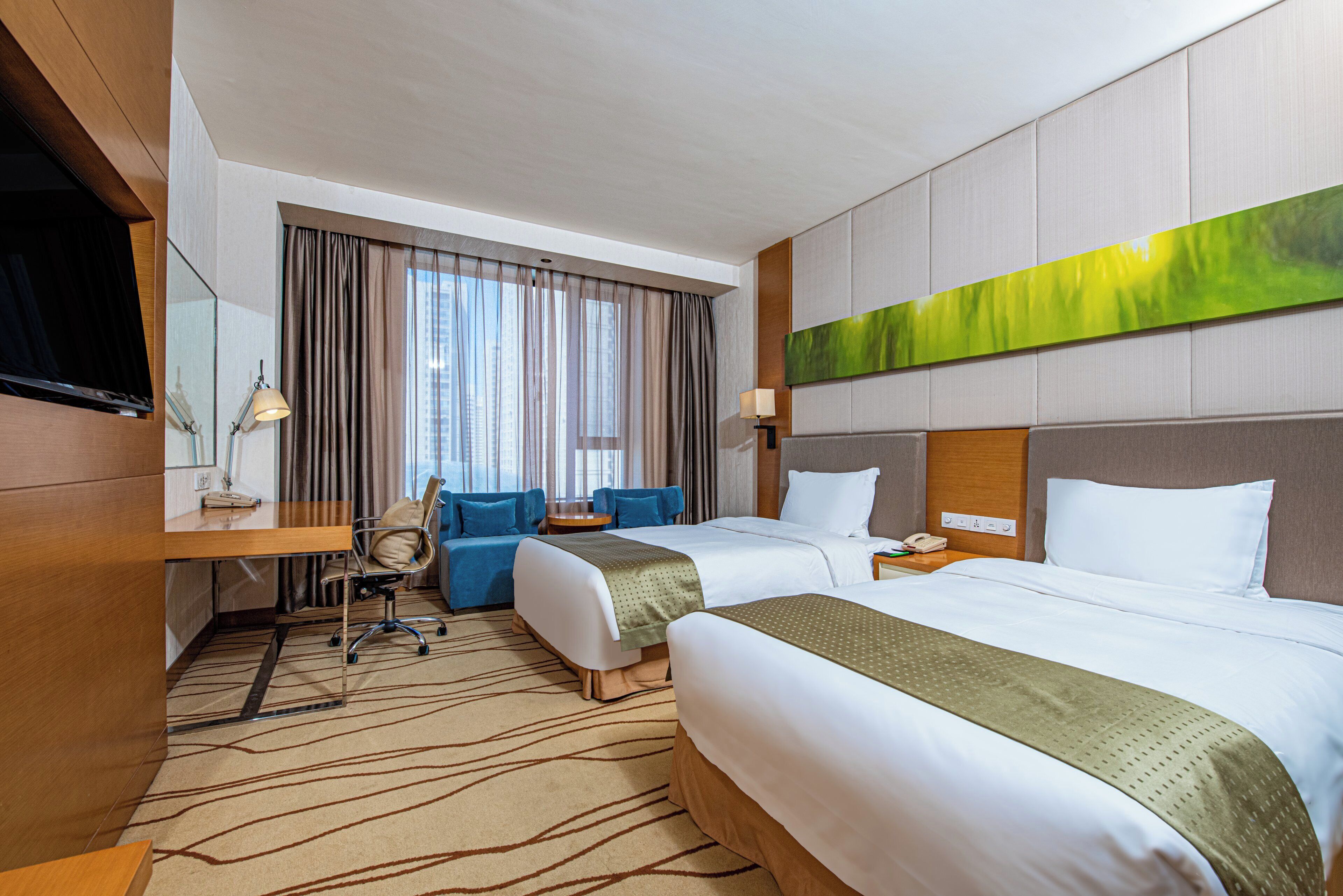 A hotel room with two beds, a desk, a chair, a television, and a large window with curtains.