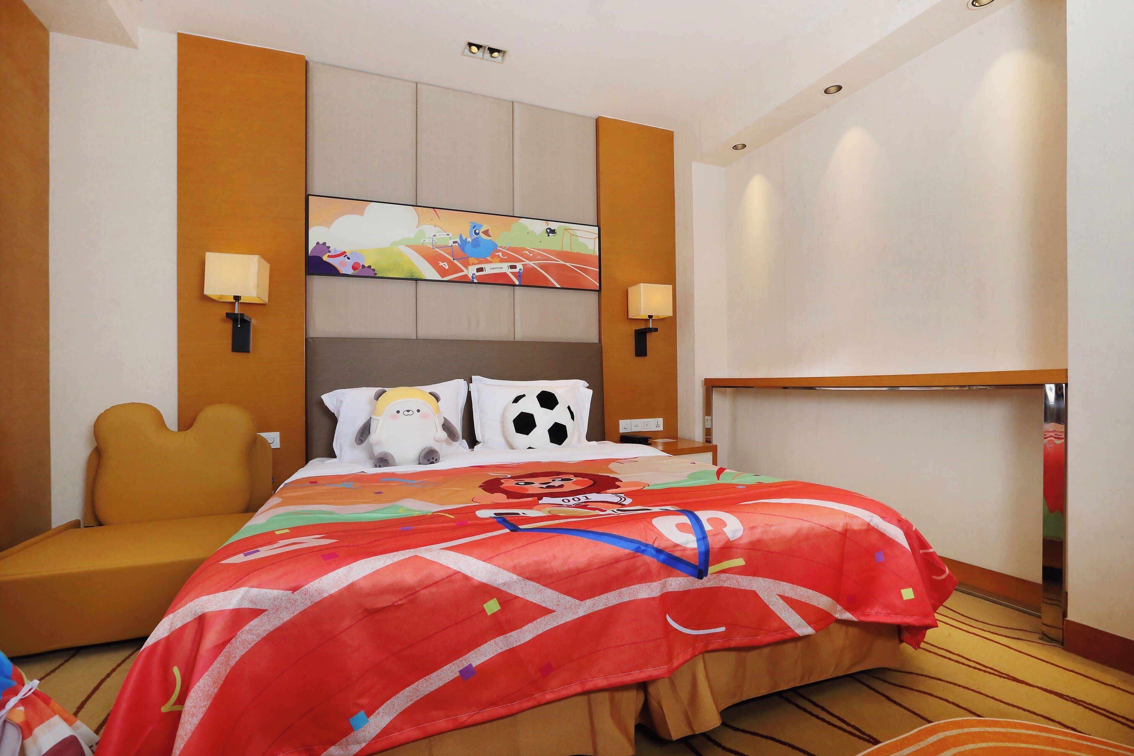 Una habitación de hotel con cama, sofá, cabecera con pintura, dos lámparas de pared y mesita de noche.