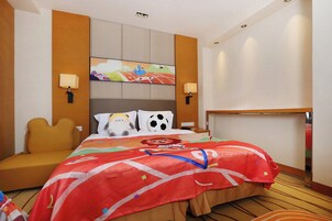 Una habitación de hotel con cama, sofá, cabecera con pintura, dos lámparas de pared y mesita de noche.