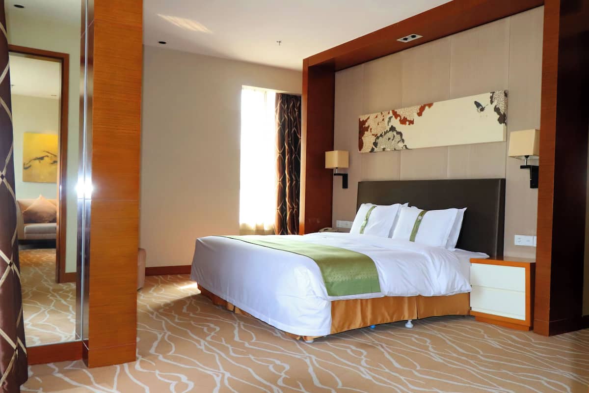 A hotel room with a large bed, a nightstand, a mirror, and a wall-mounted lamp.