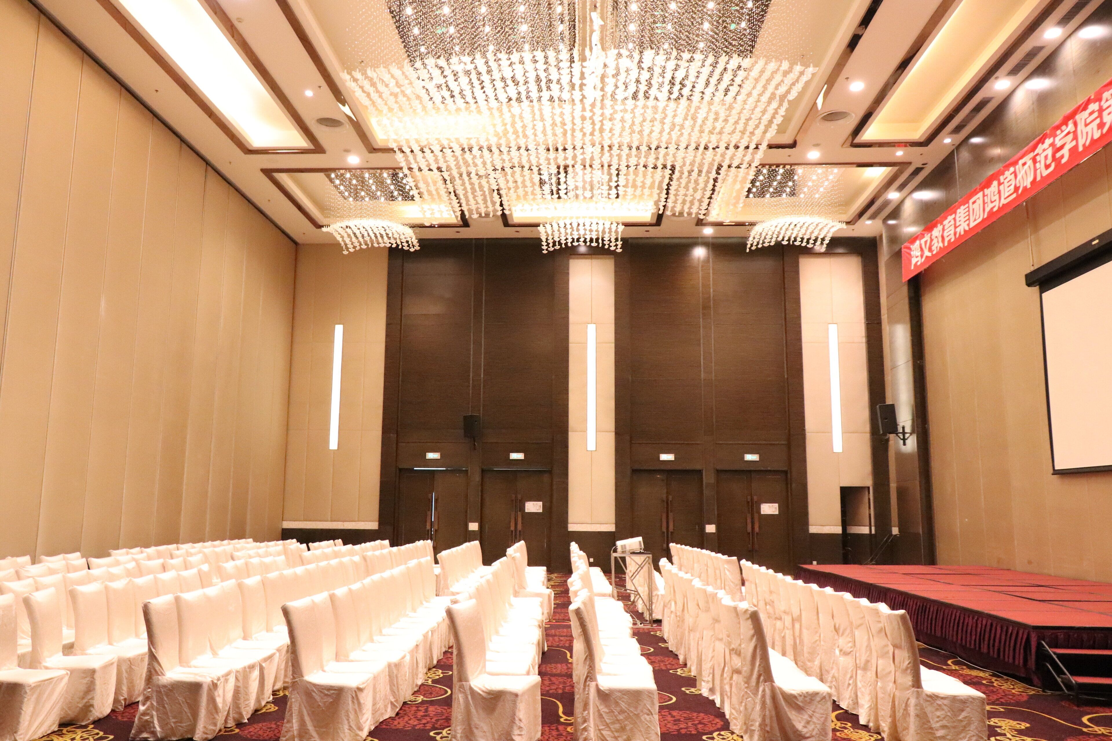 A conference room with rows of white chairs, a stage, and a large chandelier.