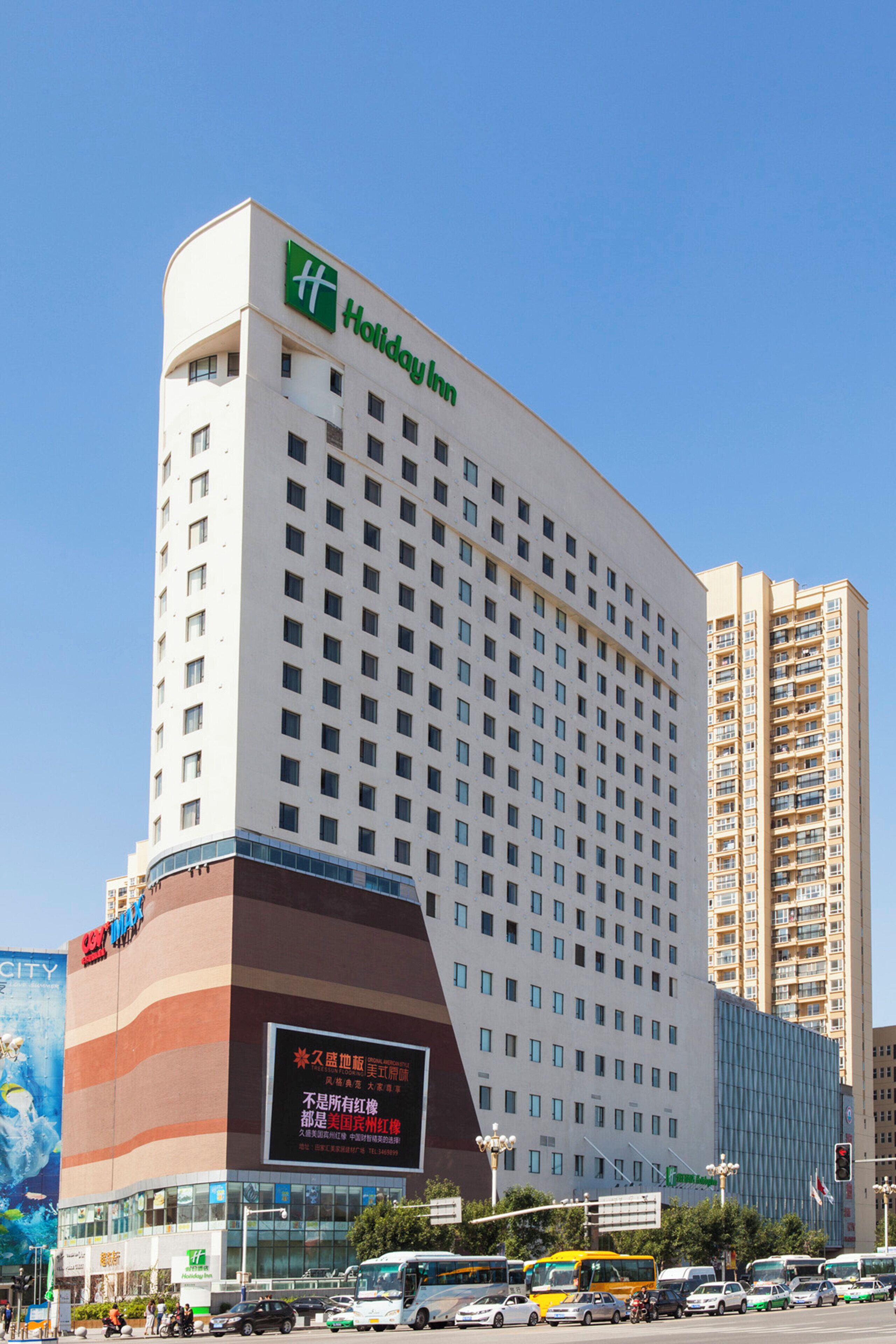 A multi-story Holiday Inn hotel with a prominent green logo, a large digital signboard, and a modern architectural design.