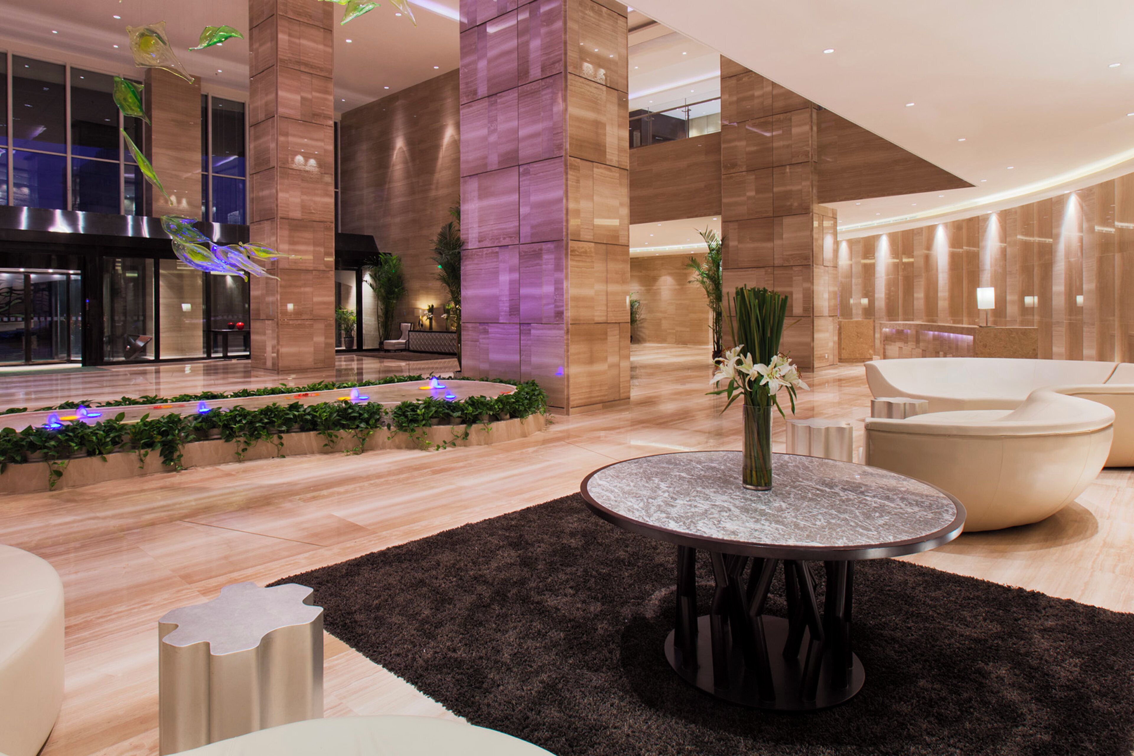 A modern lobby with a central seating area, a reception desk, and a plant arrangement.