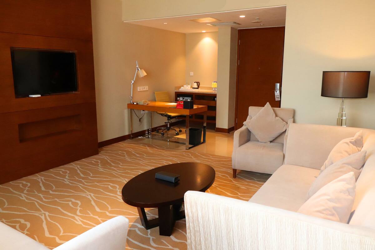 Une chambre d’hôtel comprenant un canapé, une table basse, un téléviseur fixé au mur, un bureau avec une chaise et une lampe.