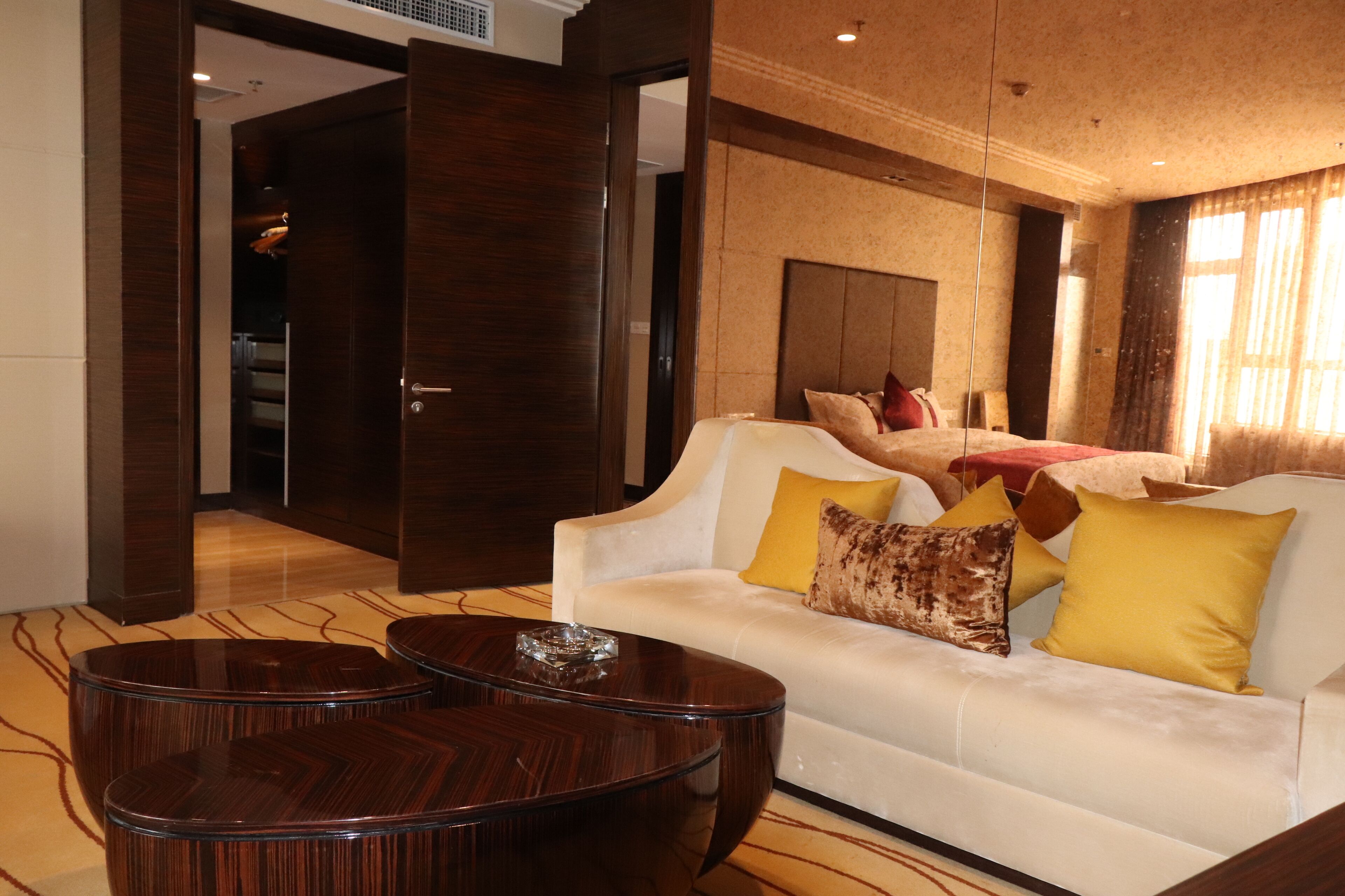 A hotel room with a white sofa, two wooden coffee tables, and a bed with multiple pillows.