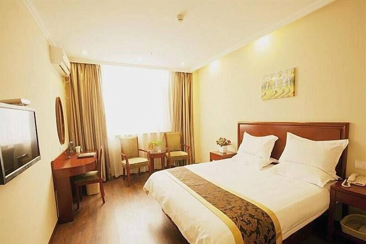 A hotel room with a large bed, a desk with a chair, a TV, and a window with curtains.
