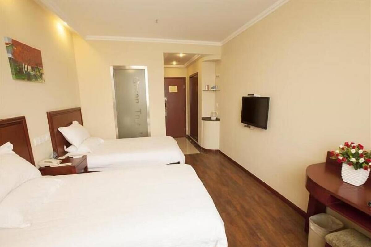 A hotel room with two beds, a TV, a desk with a vase of flowers, and a painting on the wall.